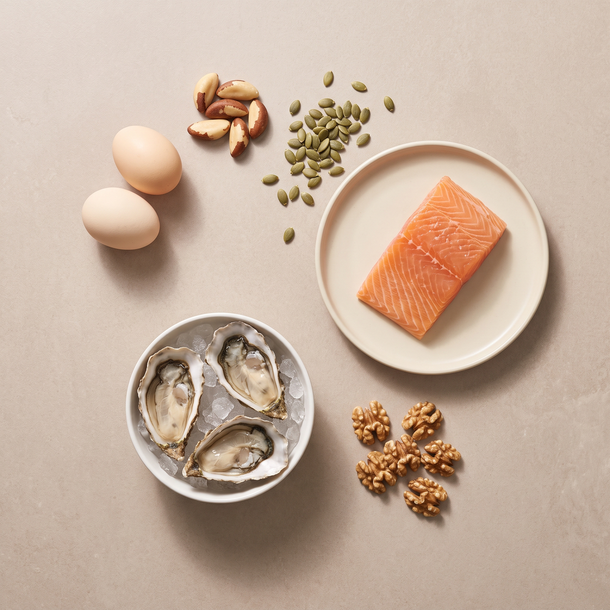 Flatlay met eieren, paranoten, pompoenpitten, zalm, oesters en walnoten op een zandkleurige ondergrond