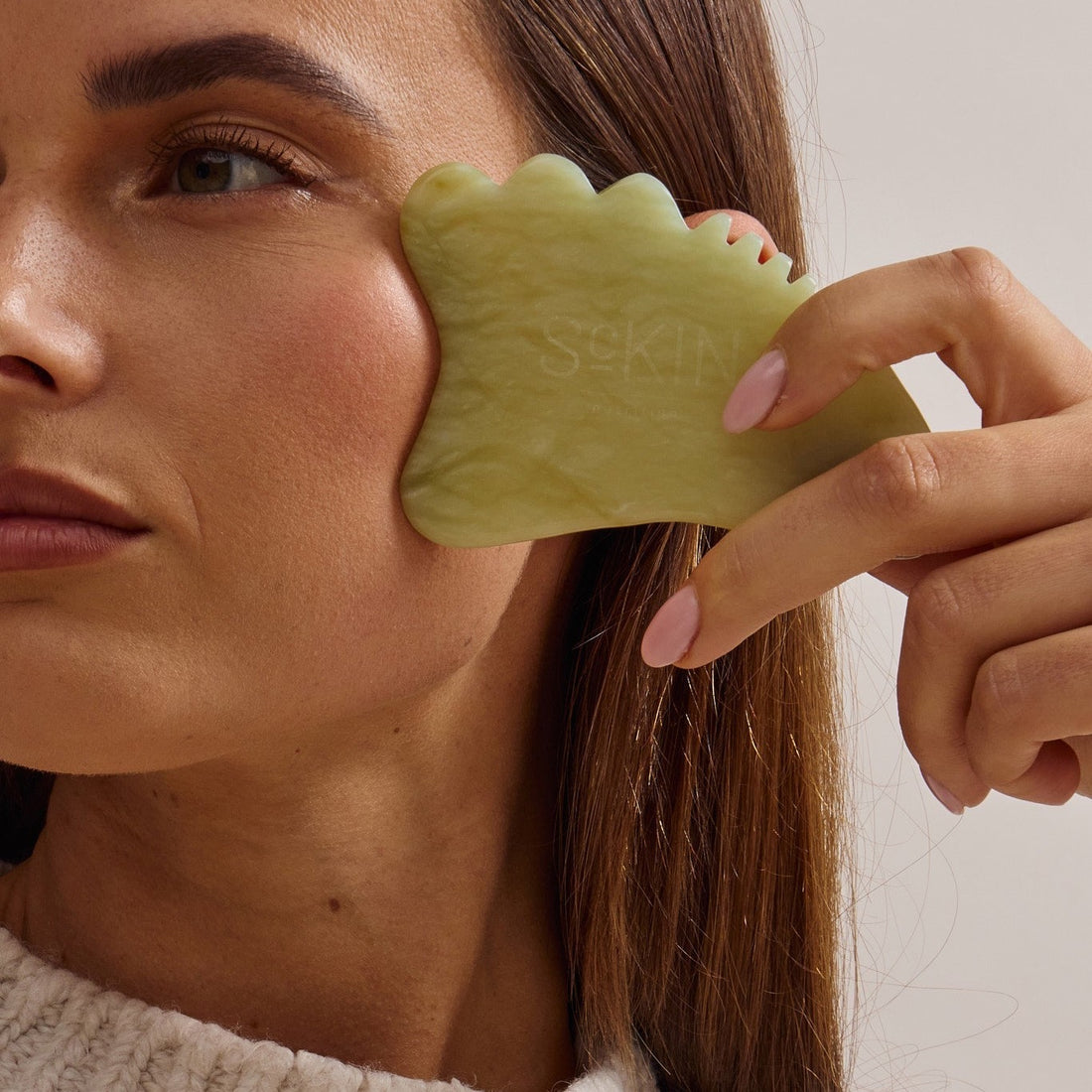 Vrouw gebruikt een jade gua sha op haar gezicht