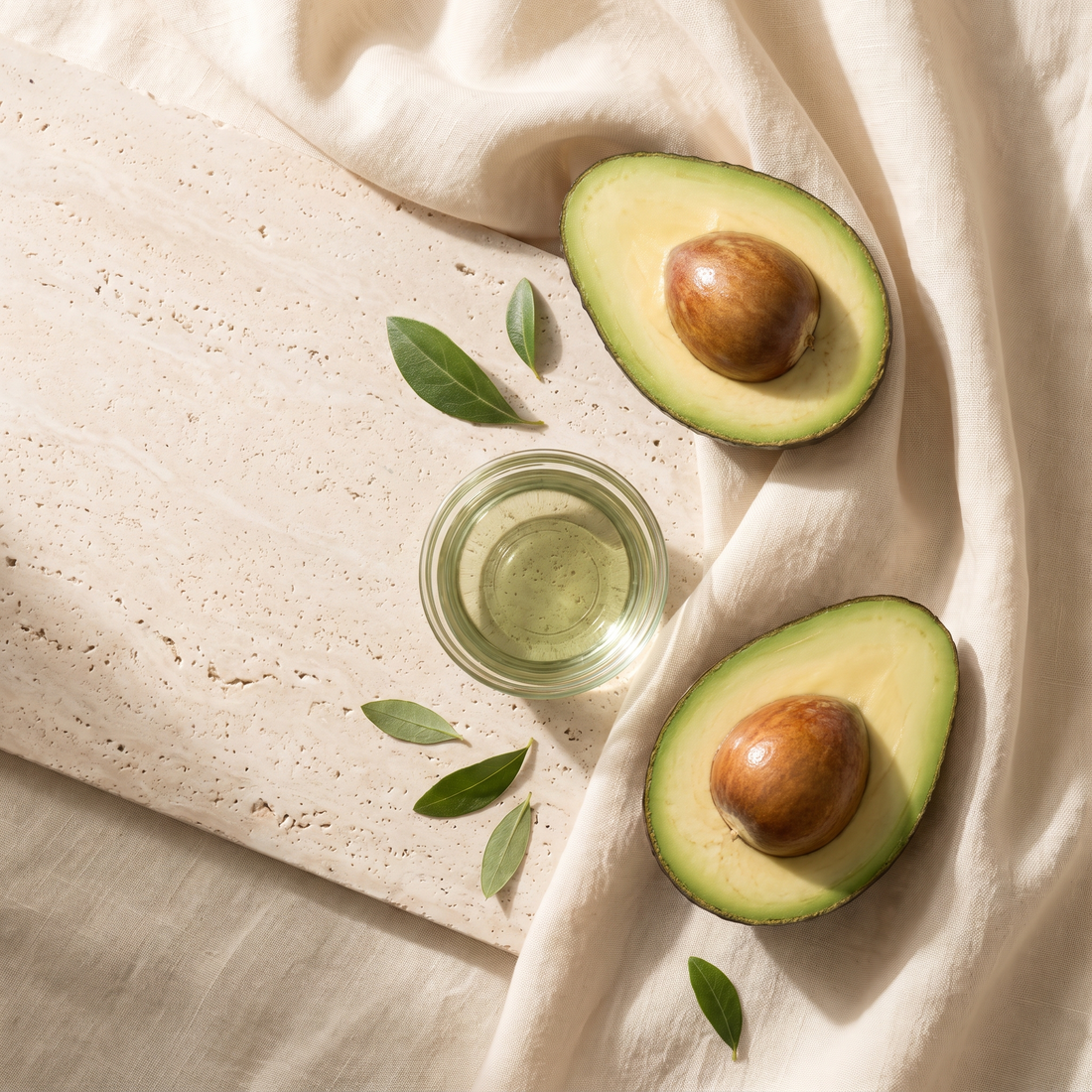 Gehalveerde avocado's en een schaal avocado-olie op travertijn met crèmekleurig linnen