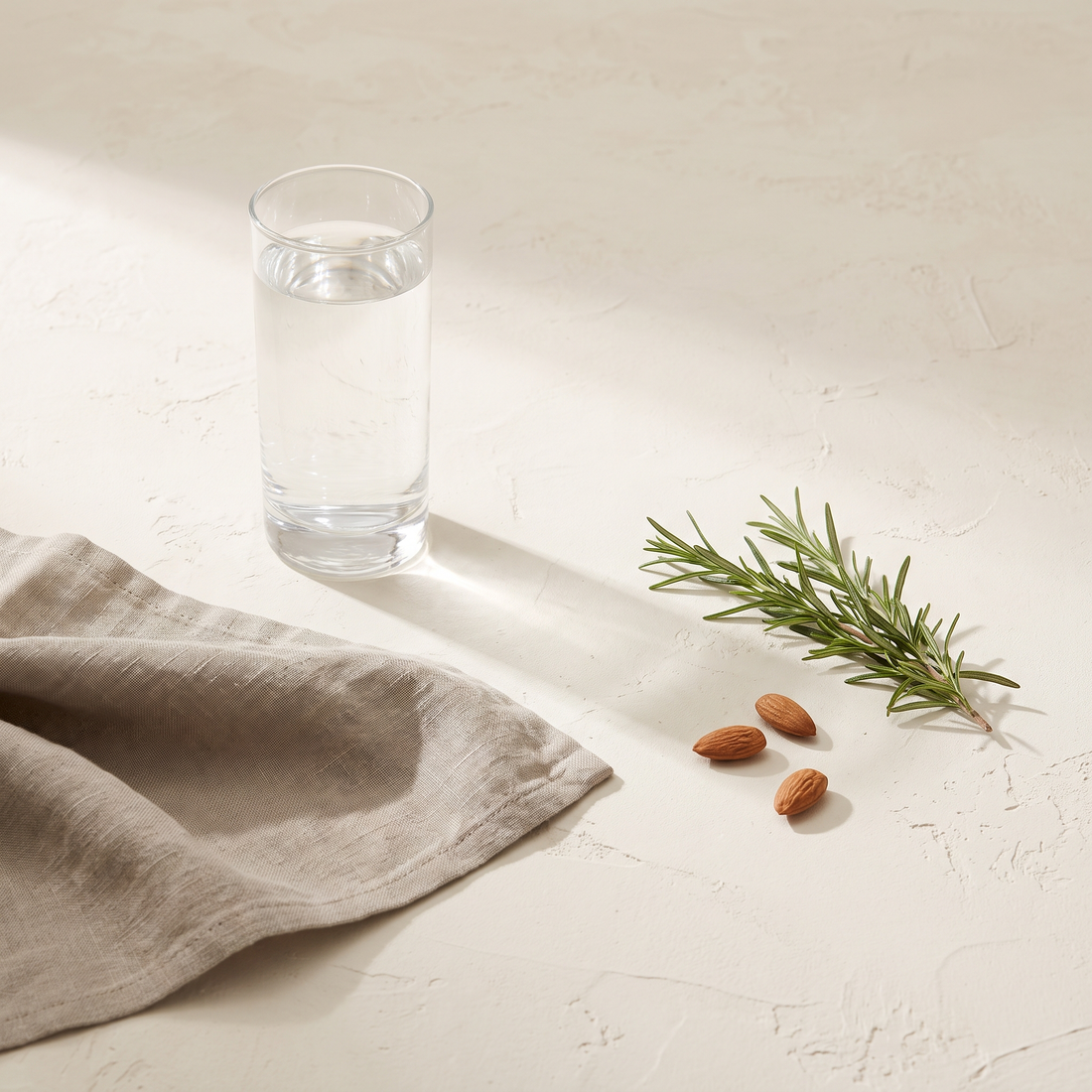 Glas water met linnen doek, verse kruiden en amandelen op een lichte ondergrond