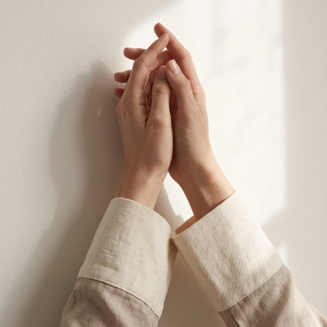 Handen rustend tegen elkaar in zacht daglicht tegen een crèmekleurige wand
