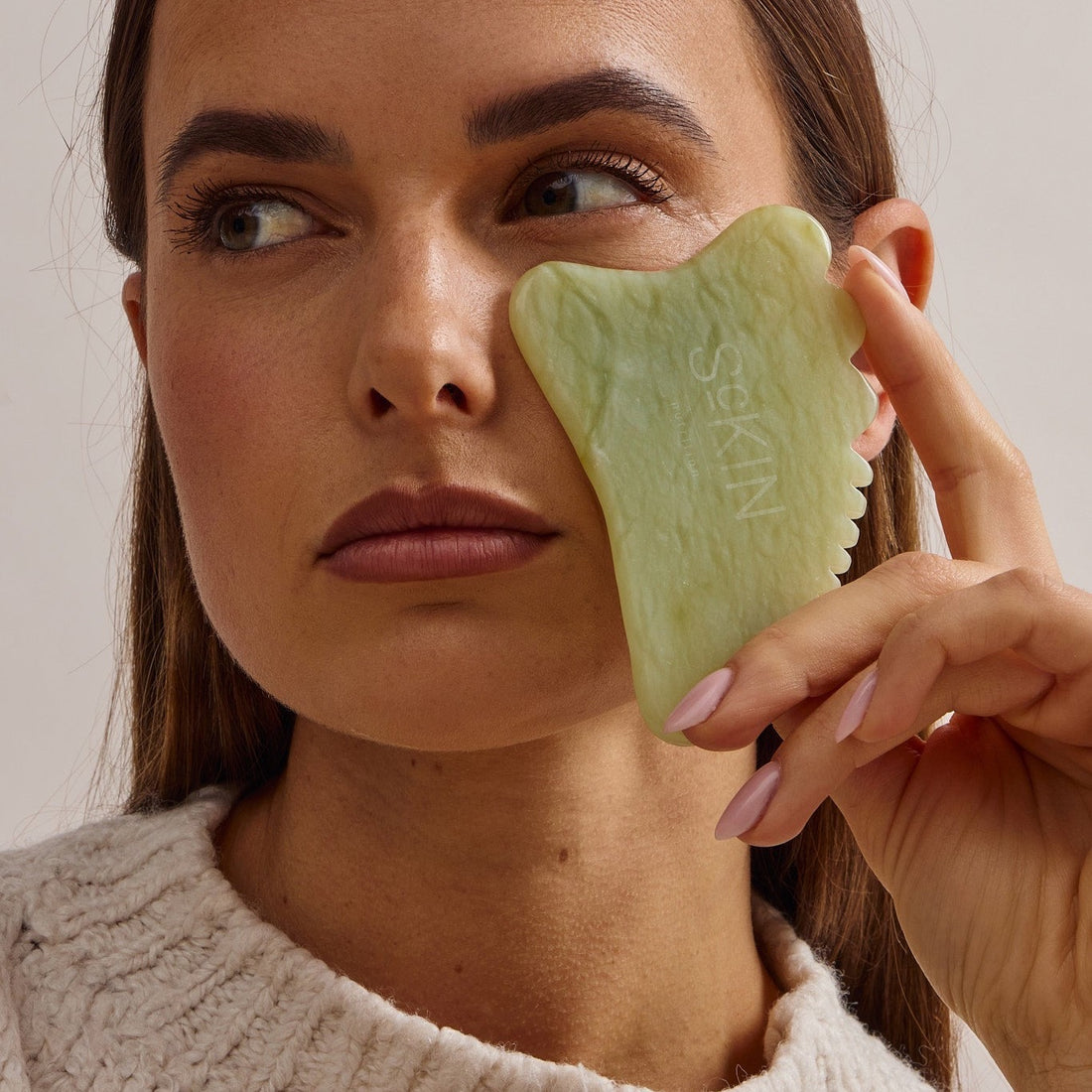 Vrouw gebruikt een koude jade gua sha onder haar oog tegen wallen